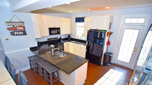 A kitchen with white cabinets, a black refrigerator, a microwave, and a coffee maker. There is a sign on the wall that says "Hooked on Fun".