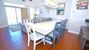 A dining room with a large glass table surrounded by blue chairs, a ceiling fan, and artwork on the walls.