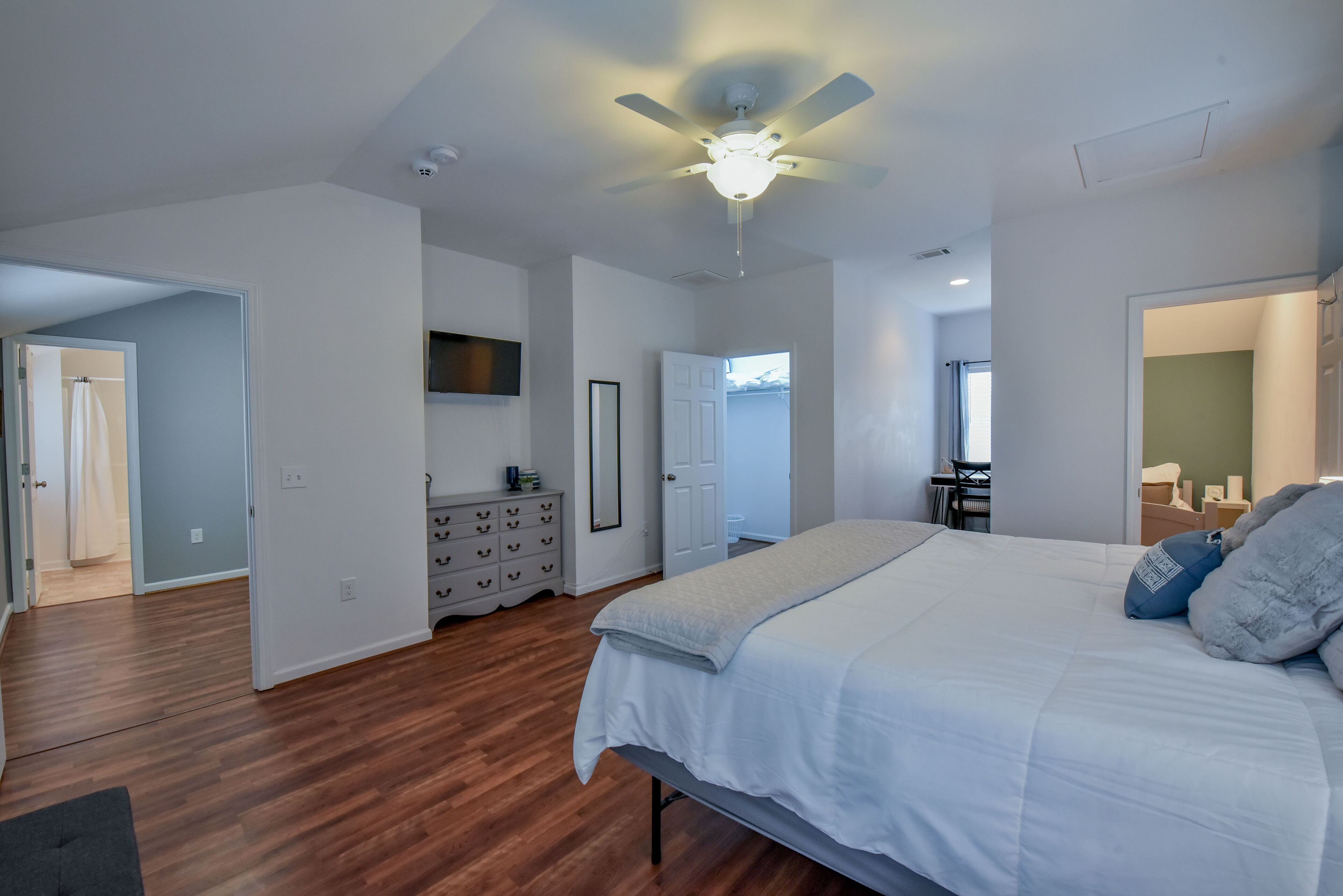 A bedroom with a large bed, a ceiling fan, and a dresser.