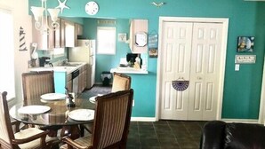 Un espacio habitable compacto con comedor, cocina y una puerta que da a otra habitación.