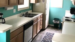 Una cocina con paredes verde azulado, armarios de madera, una encimera blanca y un letrero que dice 'Beach House'.