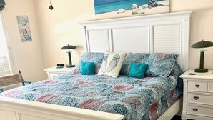 Un dormitorio con cama, mesitas de noche, ventilador de techo, obras de arte y vistas al exterior.