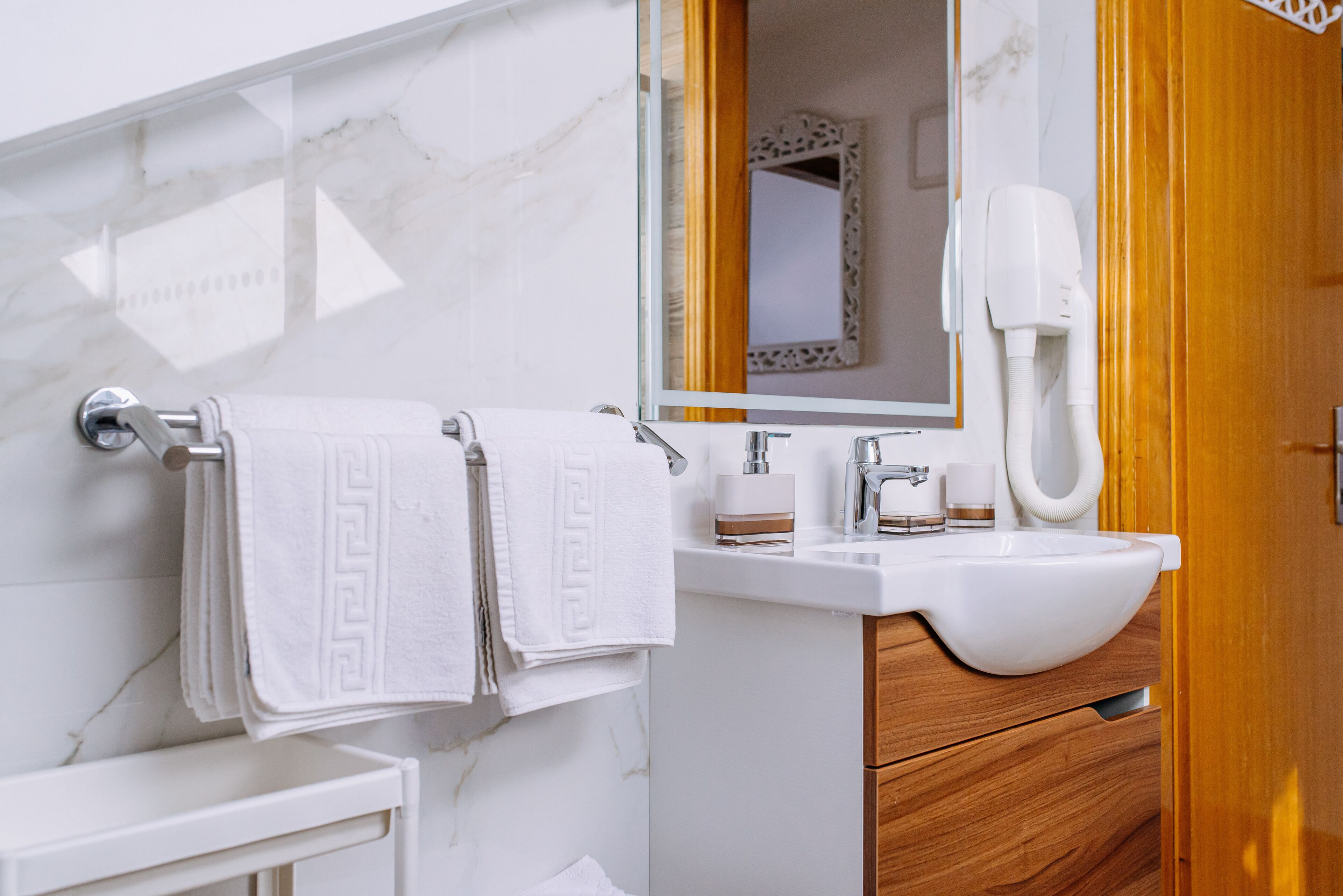 A bathroom with a marble wall, a wooden vanity, a white sink, and a towel rack with two towels.