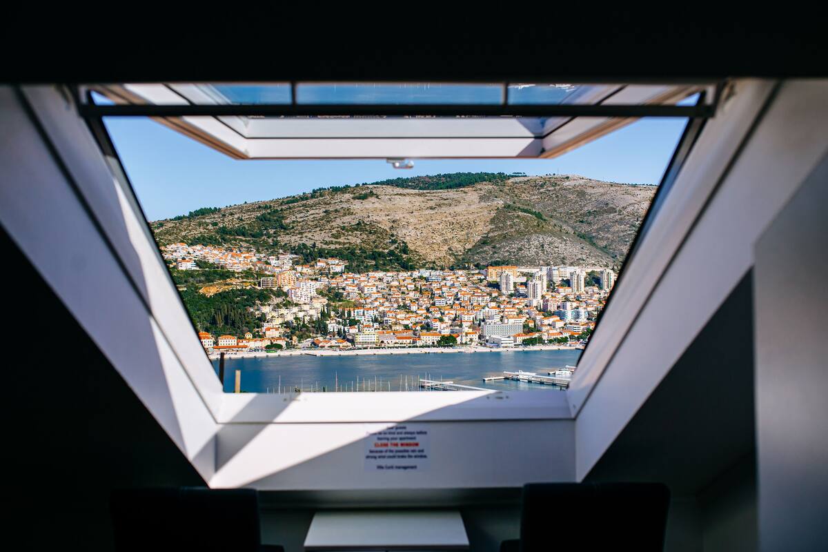A view from a window with a skylight, overlooking a coastal town with buildings and a hill.