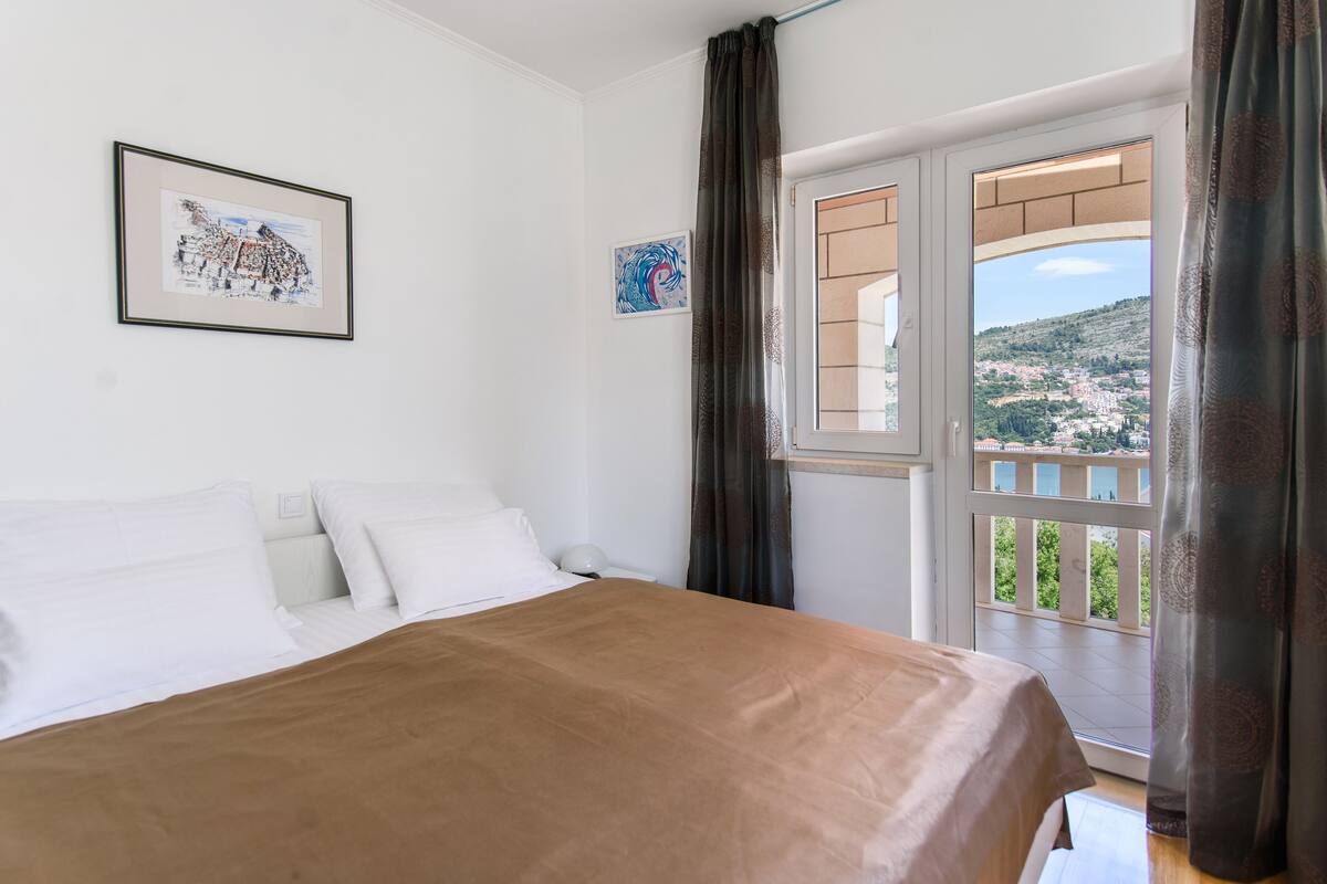 A bedroom with a bed, white walls, and a window with curtains.
