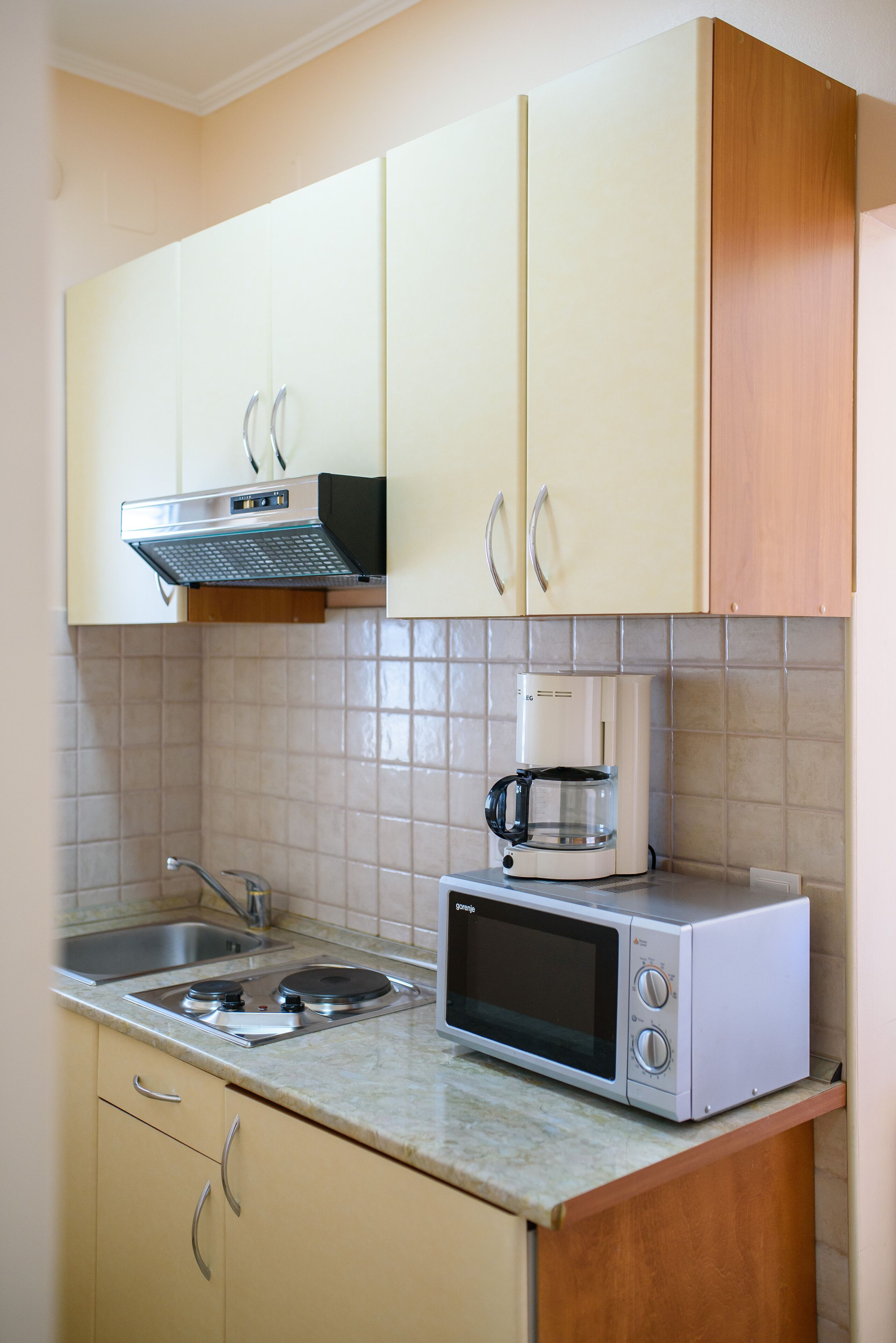 A kitchen with beige cabinets, a microwave, a coffee maker, and a sink.