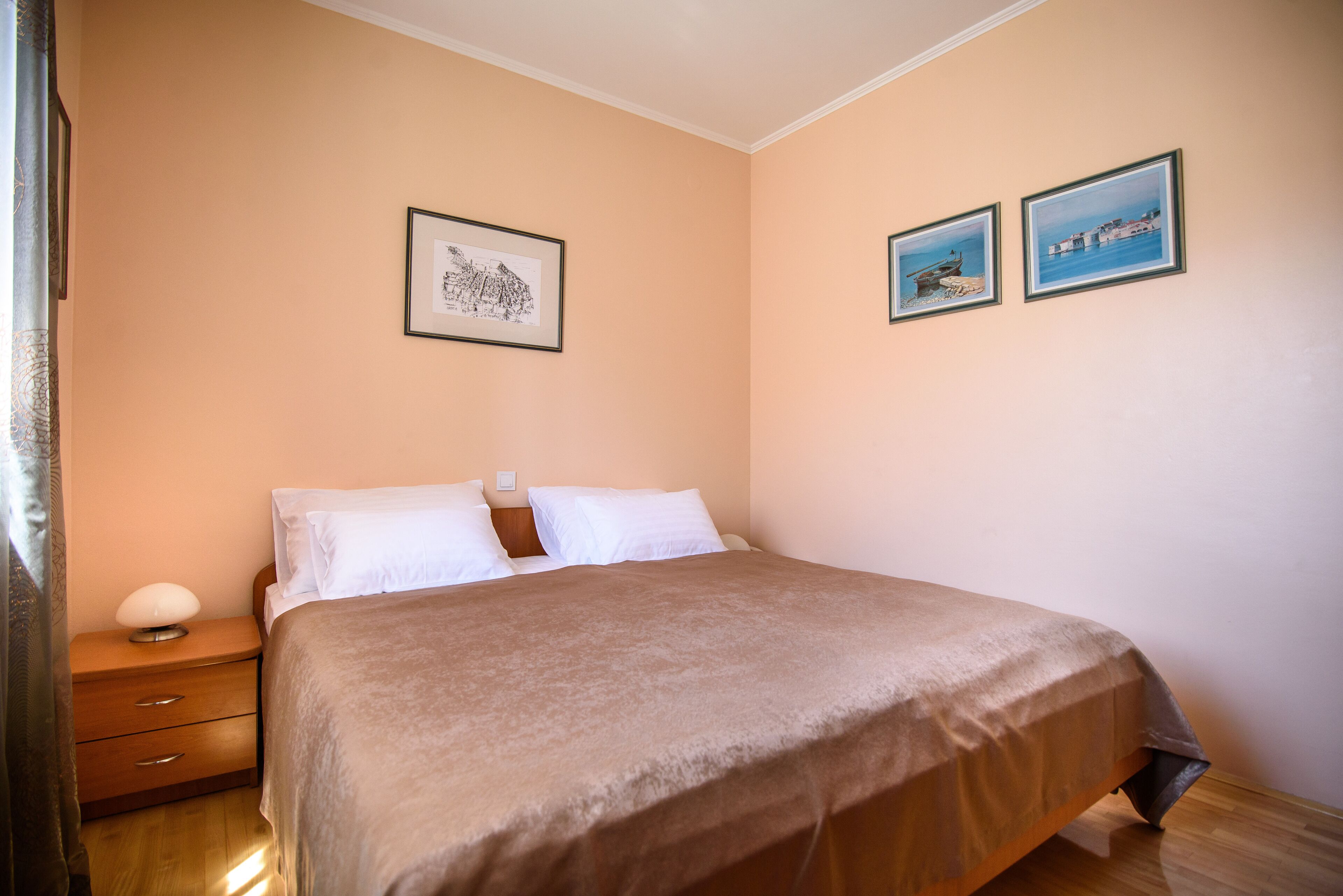 A bedroom with a bed, a nightstand, a lamp, and two framed pictures on the wall.