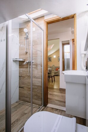 Ein modernes Badezimmer mit einer gläsernen Duschkabine, Holzboden und einem weißen Waschbecken.