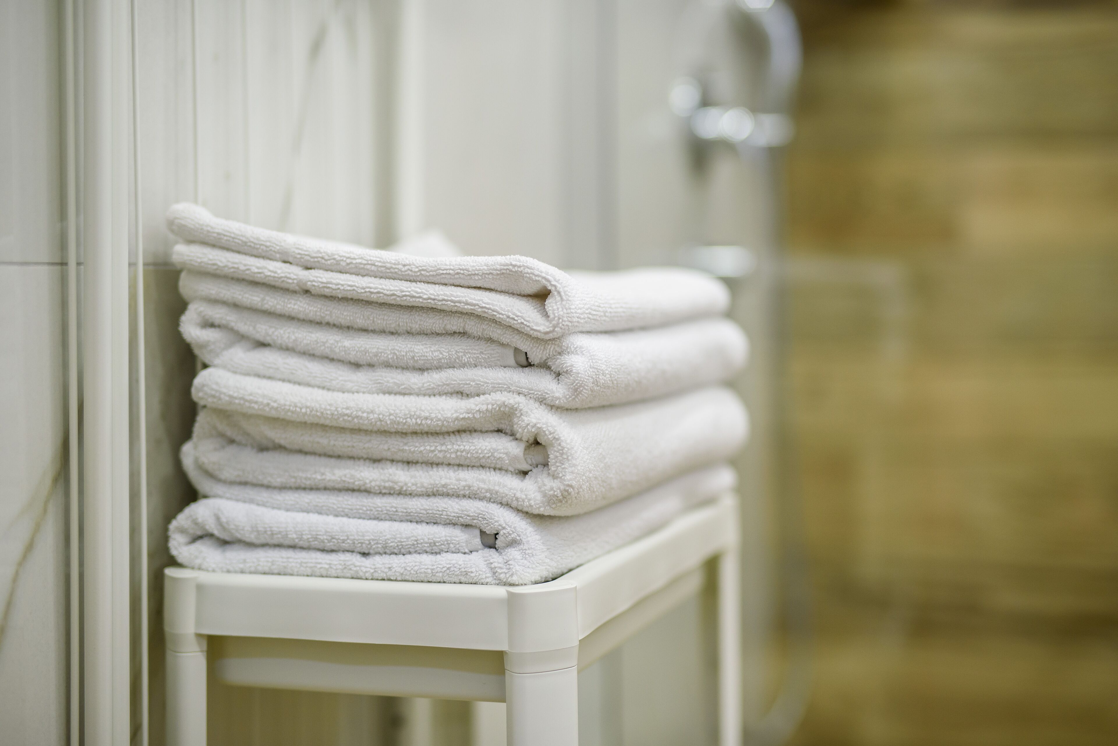 A stack of white towels on a white shelf in a bathroom.