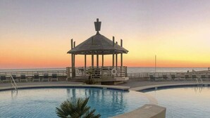 A pool with a gazebo, palm trees, and a sunset view. - Oceanfront 3BR w/ Incredible Views+Balcony+Pools (Orange Beach)