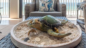 A turtle on a sandy beach with a chair and a view of the sea in the background. - Oceanfront 3BR w/ Incredible Views+Balcony+Pools (Orange Beach)