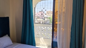 Habitación de hotel con cama, ventilador de techo y vista al balcón exterior.