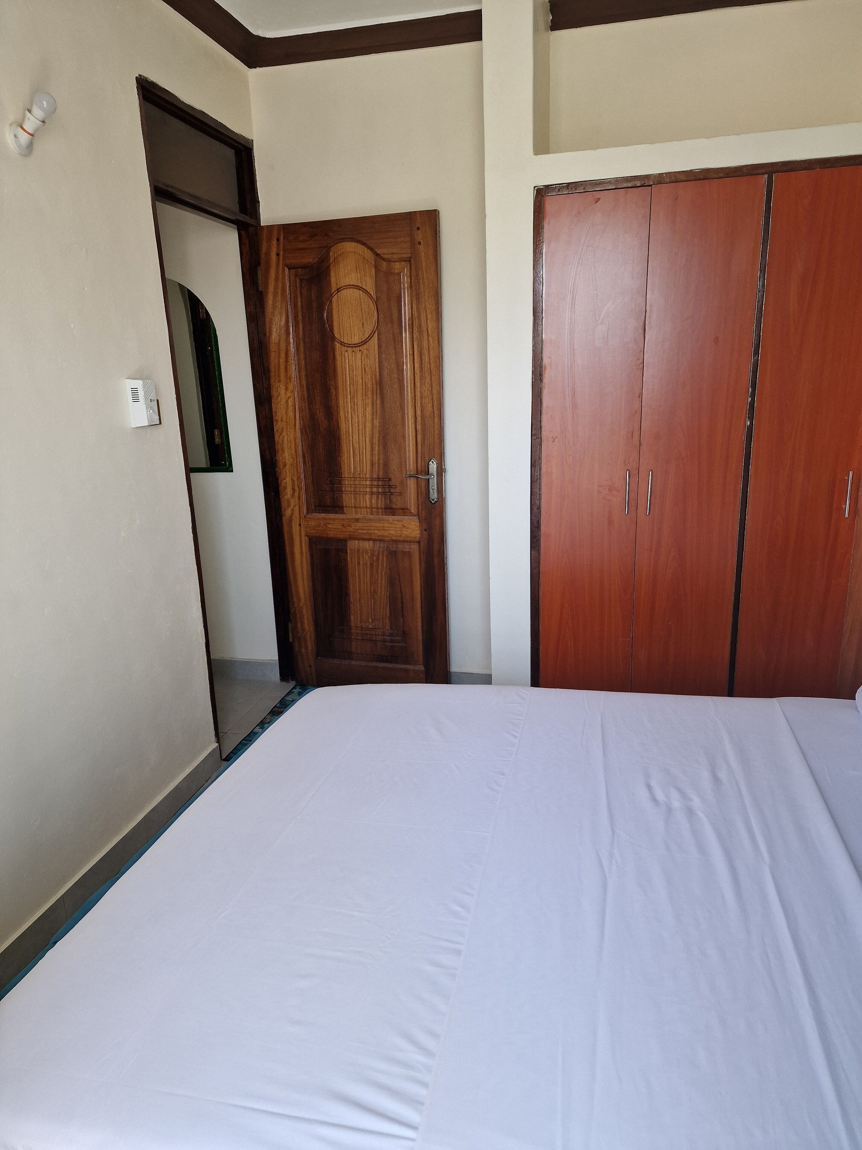 A bedroom with a wooden wardrobe, a bed with white bedding, and a door with a circular design.