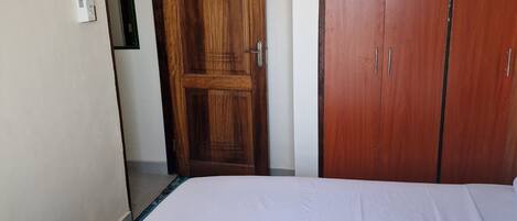 A bedroom with a wooden wardrobe, a bed with white bedding, and a door with a circular design.