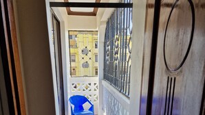 Pasillo que conduce a un balcón con sillas de plástico azules y una pared amarilla con estampado.