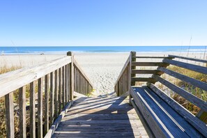 A wooden boardwalk leading to a beach with a clear view of the ocean.