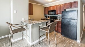 A kitchen with a central island, two bar stools, wooden cabinets, a black refrigerator, and a microwave. - Oceanfront 2 BR Condo with a Shared Pool! Channel Marker 204 (Surfside Beach)