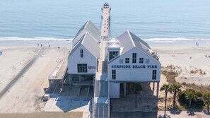 Un bâtiment blanc avec une enseigne indiquant « SURFSIDE BEACH PIER » se trouve sur la plage.