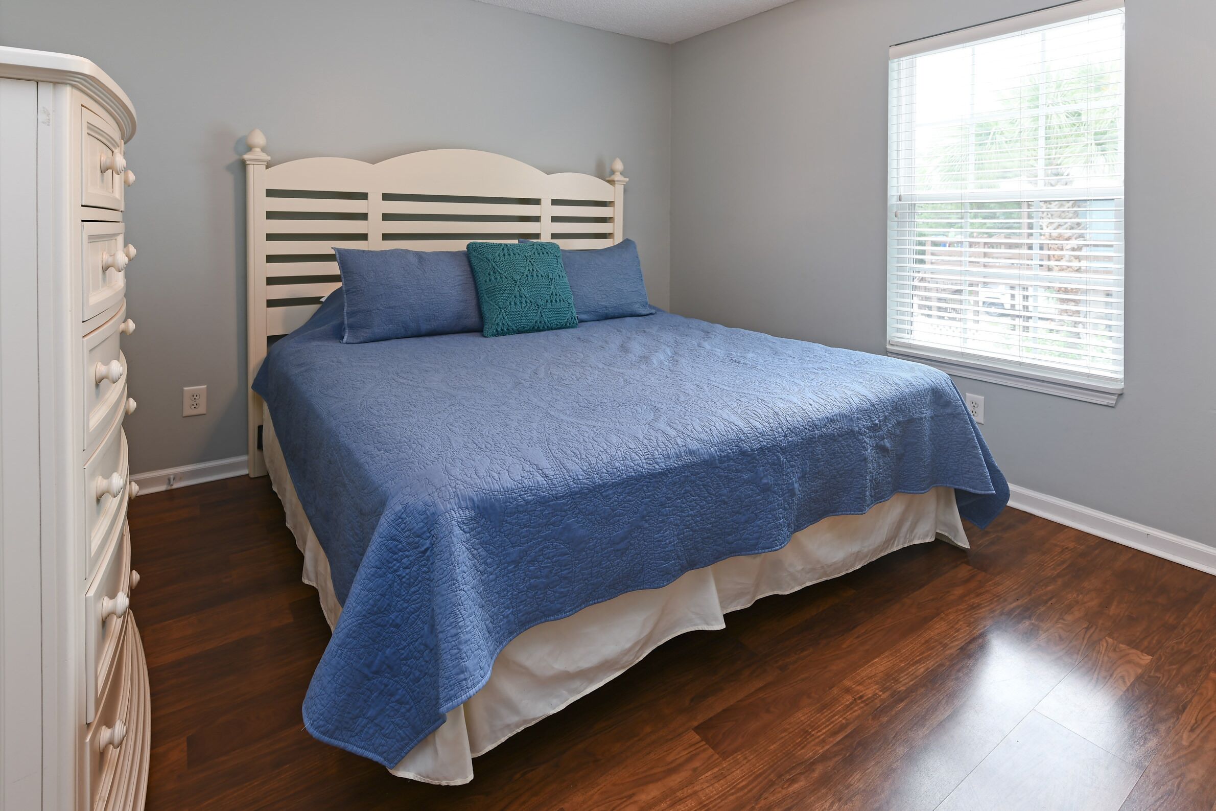 A bedroom with a bed, a dresser, and a window with blinds.