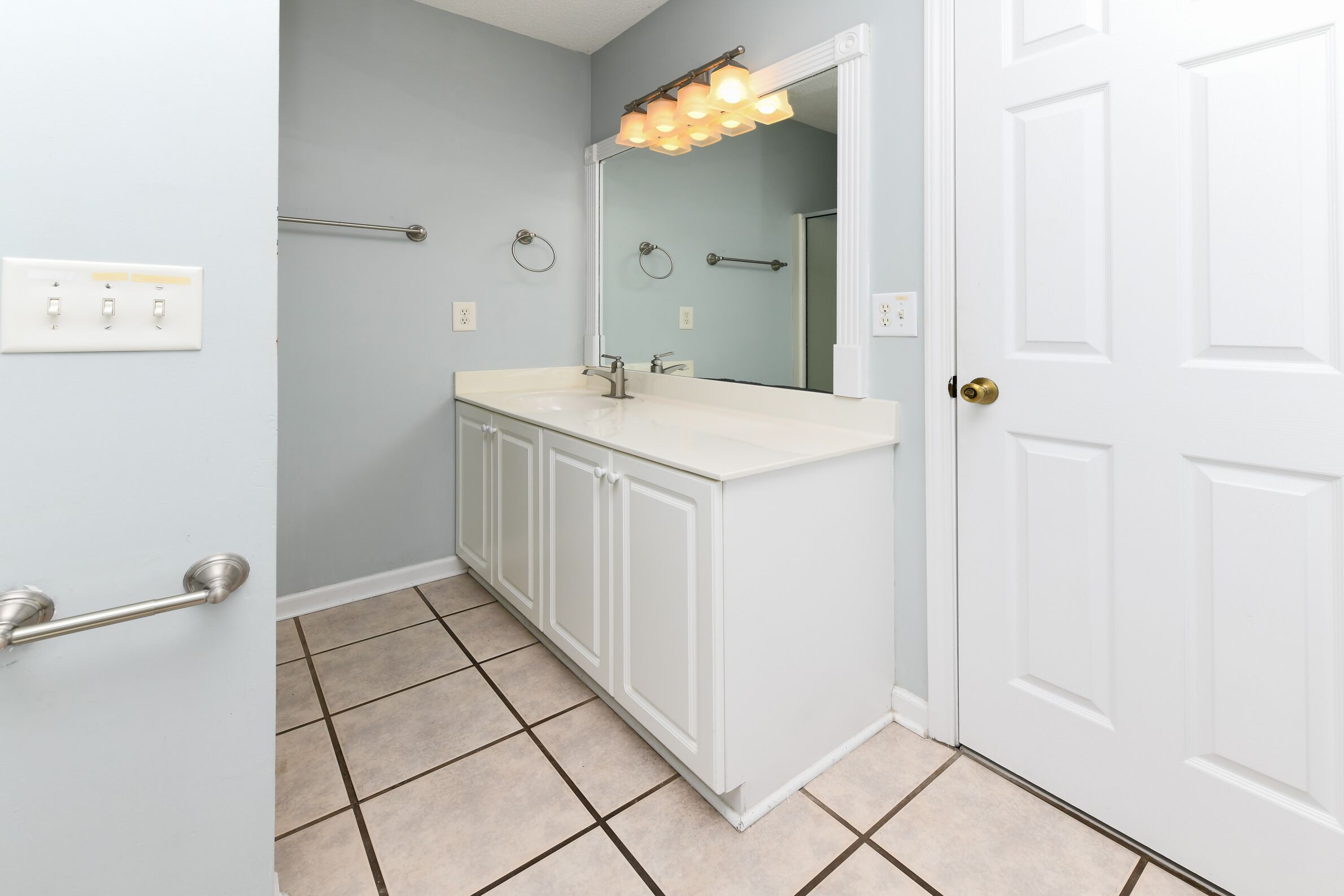 Une salle de bain avec un meuble-lavabo blanc, un miroir et un luminaire placé au-dessus du miroir.