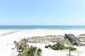 A beach with white sand, a wooden staircase leading to a structure, and a clear blue sky.
