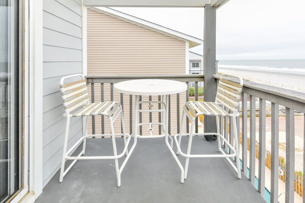 Un balcon avec une table ronde et deux chaises à rayures, donnant sur une plage.
