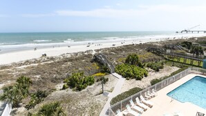 Blick auf einen Strand mit Poolbereich, einer Pier und einem Fußweg.