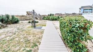 Ein hölzerner Weg führt zu einem Strandbereich mit einem Fahrradständer und einer Treppe zu einem Strandhaus.