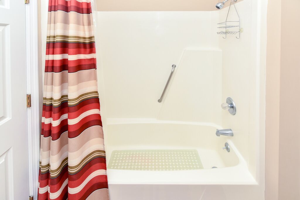 A bathroom with a white bathtub, a showerhead, and a striped shower curtain.