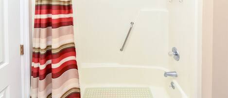 A bathroom with a white bathtub, a showerhead, and a striped shower curtain.