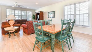 A dining area with a wooden table and green chairs, a sofa, a lamp, and a bookshelf. - 2nd Row 4 BR Beach House! Dream Weaver (Surfside Beach)