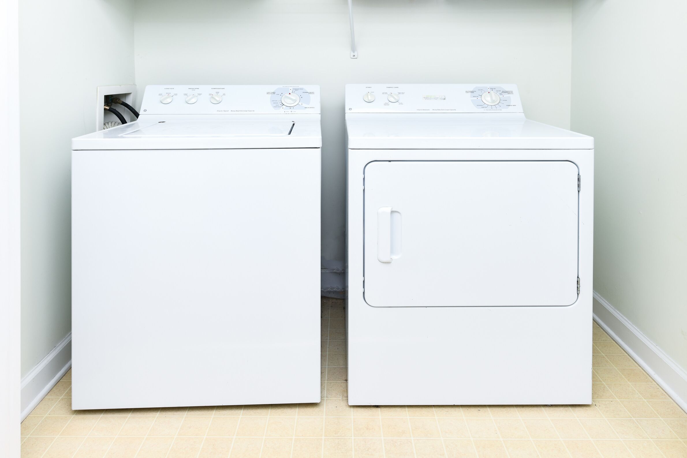 Dos lavadoras blancas de carga frontal en un cuarto de lavado con piso de baldosas.