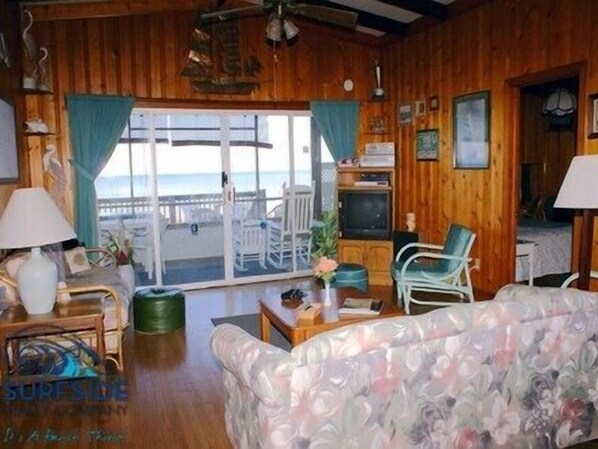 A wooden interior with a sofa, chairs, a television, and a view through a glass door to the outside.