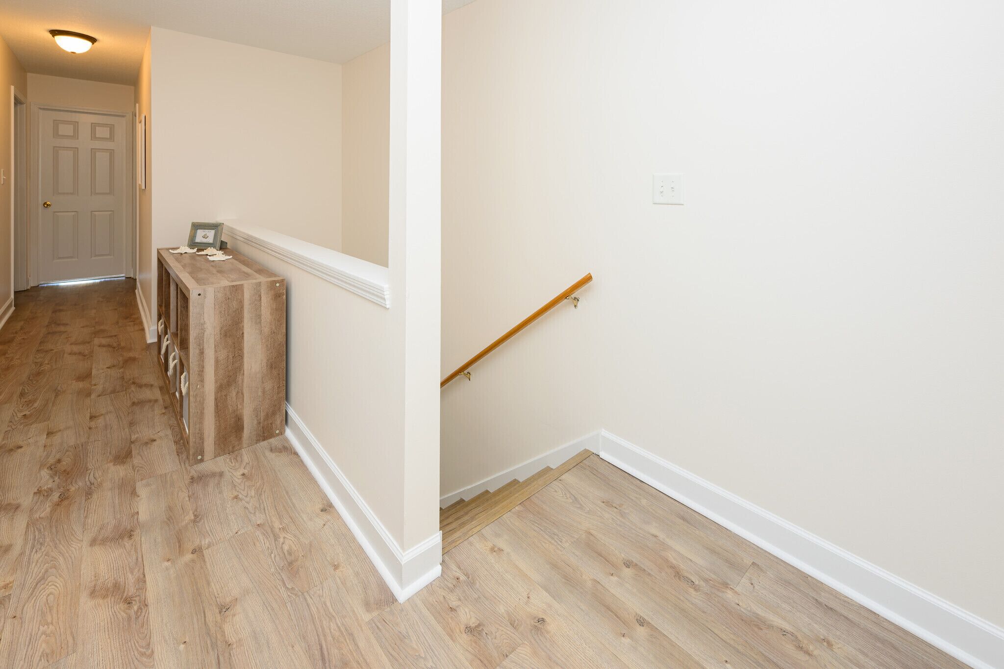 A hallway with wooden flooring, white walls, and a wooden bench.