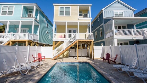 A pool area with lounge chairs and a staircase leading to a multi-level building.