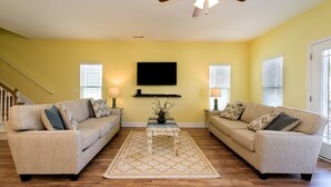 A living room with two beige sofas, a coffee table, and a TV mounted on the wall.