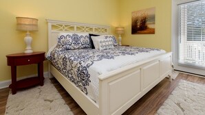 A bedroom with a white bed, two bedside tables, and a window with blinds.