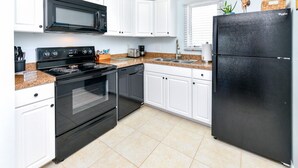 A kitchen with white cabinets, a black refrigerator, a microwave, a stove, and a dishwasher.