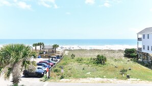 Blick auf einen Strand mit einem Parkplatz, einer Holzkonstruktion und einem weißen Gebäude mit Balkon mit Meerblick.