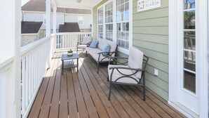 Eine überdachte Veranda mit Holzdeck, einer Couch mit Kissen, einem kleinen Tisch und einem Schild mit der Aufschrift 'STELLA MARIS'.