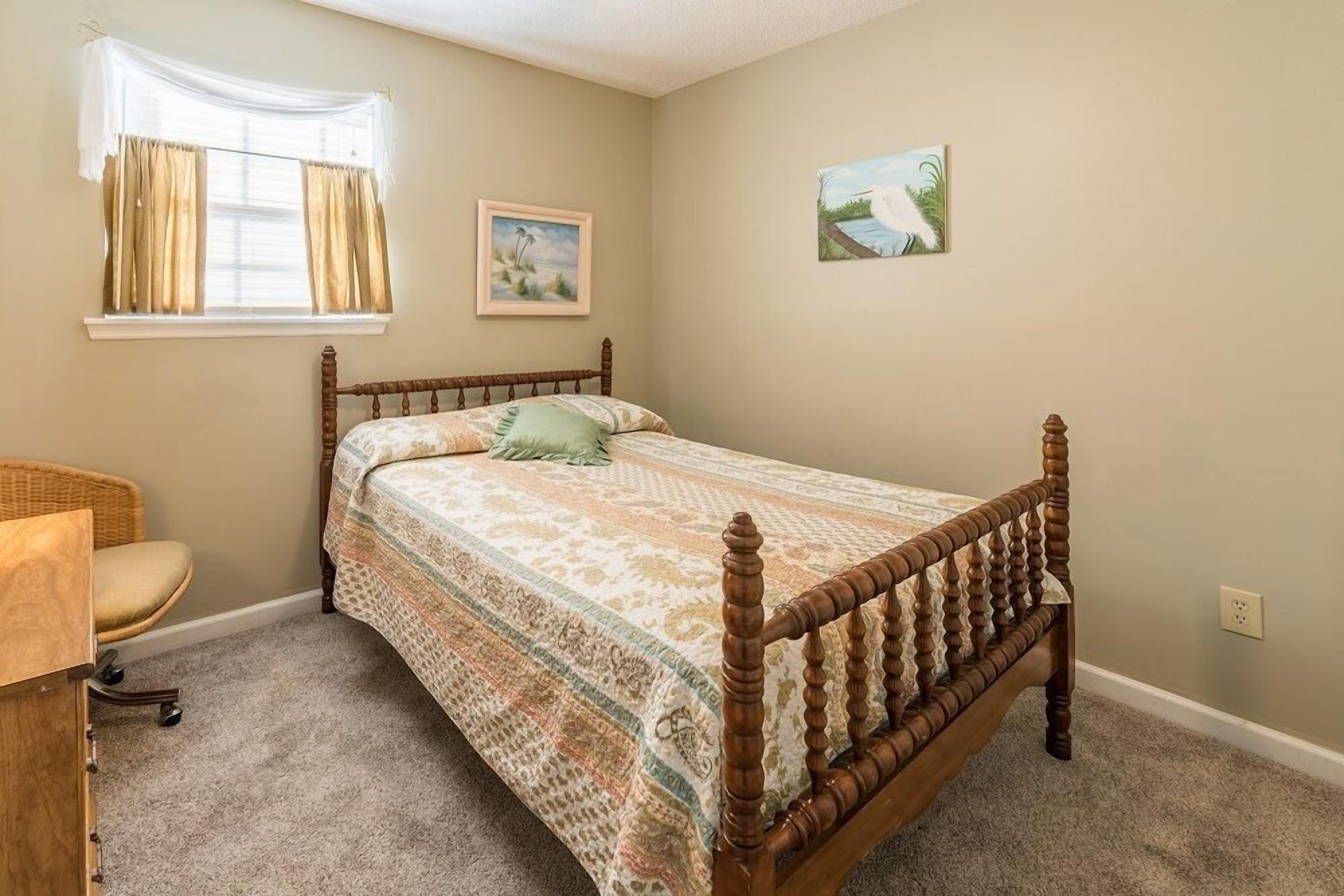 A bedroom with a wooden bed, a wicker chair, a desk, and a window with curtains.