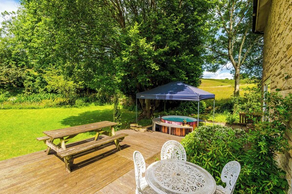 A wooden deck with picnic tables and chairs, a hot tub, and a covered area.
