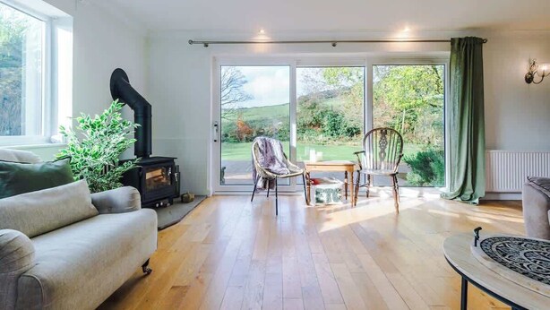 Een woonkamer met een bank, een tafel, een stoel, een open haard en uitzicht door een glazen deur.