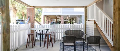 En overdækket terrasse med hvidt plankeværk, en murstenssøjle og et bord med fire stole.