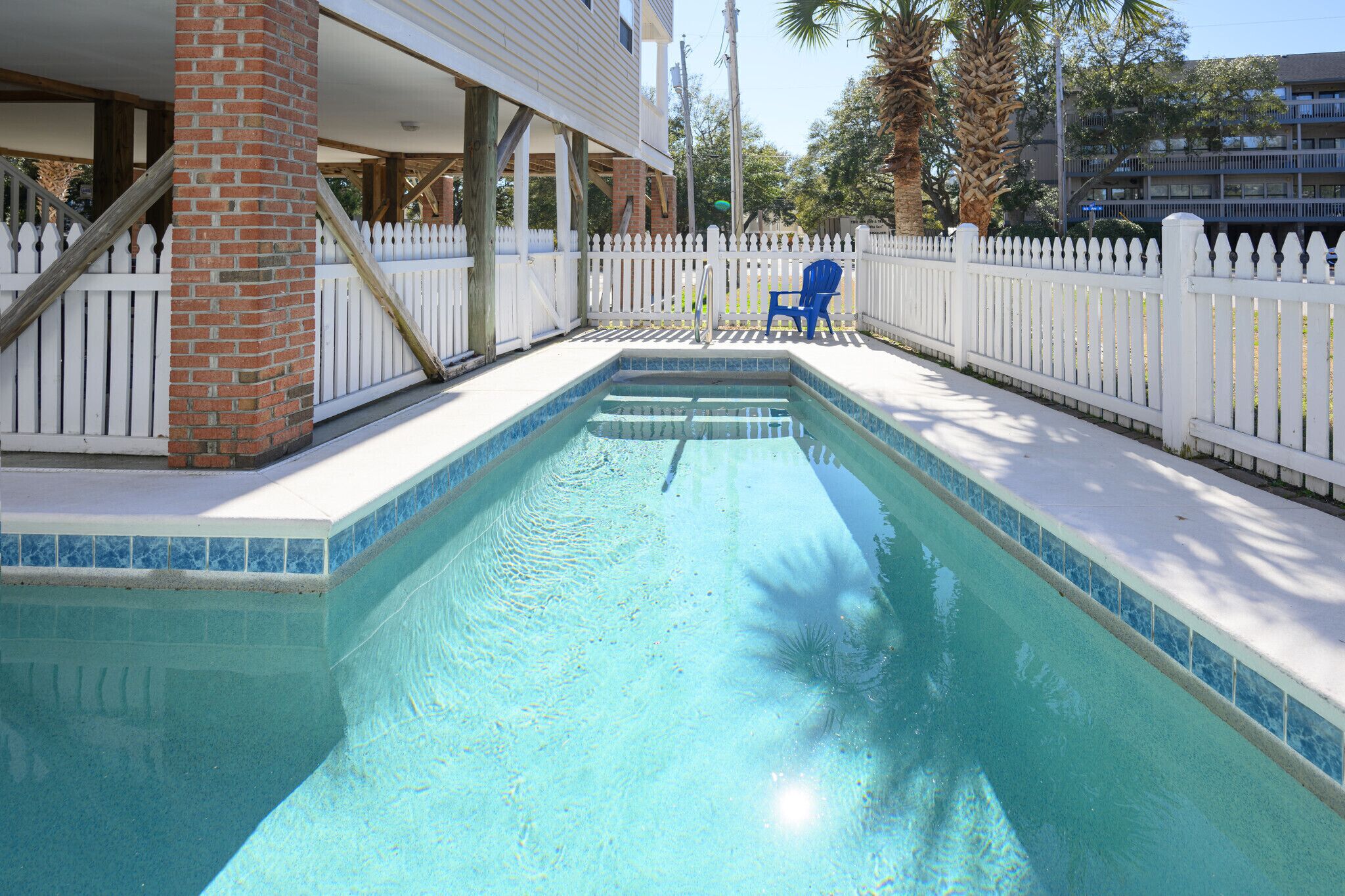 Une piscine rectangulaire entourée d’une clôture blanche en bois et agrémentée d’une chaise bleue.
