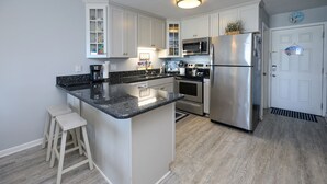 A modern kitchen with white cabinets, a stainless steel refrigerator, and a granite countertop. - Oceanfront 2 BR with a Shared Pool! Sea Cloisters I 204B (Surfside Beach)