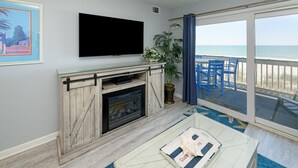 A living room with a fireplace, a flat-screen TV, and a view of the beach. - Oceanfront 2 BR with a Shared Pool! Sea Cloisters I 204B (Surfside Beach)