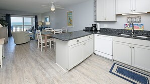 A modern kitchen with white cabinets, a granite countertop, and a view to the outside. - Oceanfront 2 BR with a Shared Pool! Sea Cloisters I 204B (Surfside Beach)