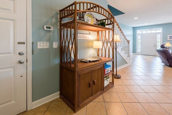 Une console en bois, ornée d’une horloge, d’une lampe et d’une petite étagère où sont posés des livres et des objets décoratifs, se trouve dans un couloir dont le sol est carrelé et un des murs est bleu.
