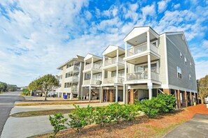 A multi-story residential building with balconies, a covered parking area, and a landscaped front yard.